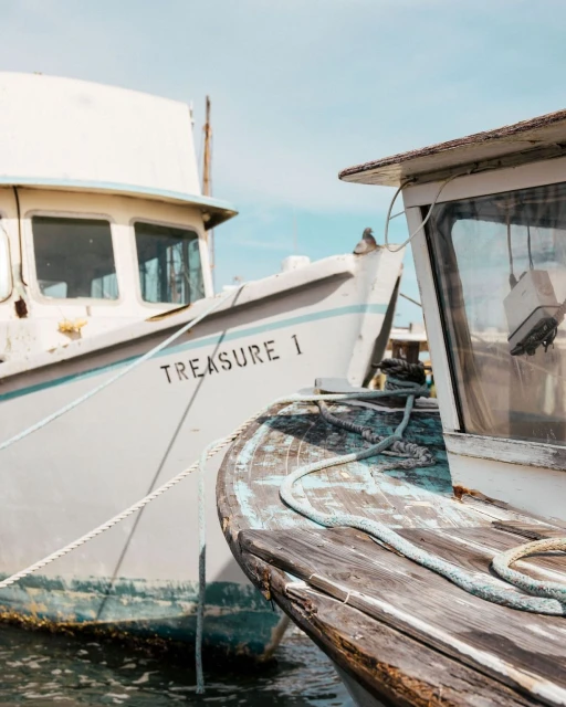 Two docked vintage fishing boats, one labeled 'Treasure 1,' are captured in a close-up shot with cloudy skies in the background.