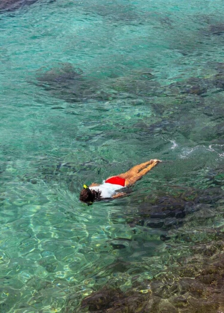 Woman swims in turquoise water wearing a snorkel and red shorts, capturing an aquatic adventure in a tropical setting near the coastline.