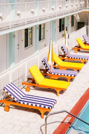 Row of yellow and blue striped sun loungers beside a bright motel pool deck photographed by Amanda Julca.