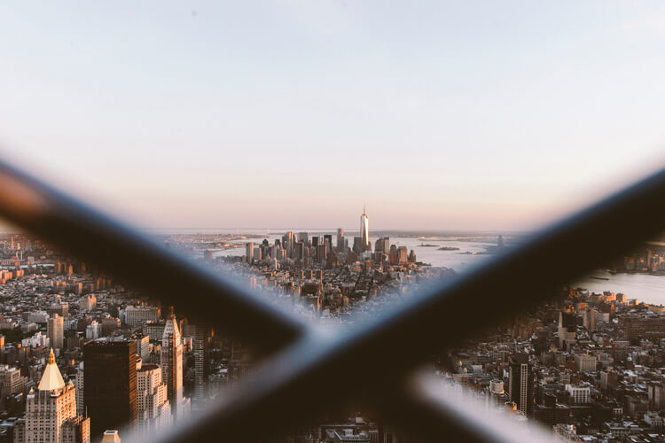 Cityscape view of New York City skyline with the One World Trade Center building in view, seen through a foreground metal structure.