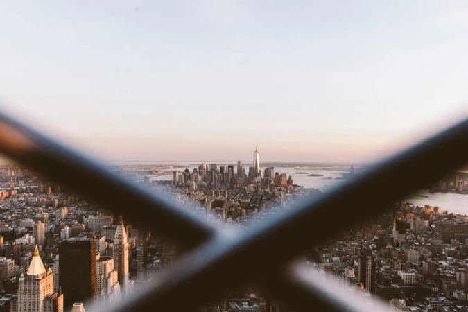 Cityscape view of New York City skyline with the One World Trade Center building in view, seen through a foreground metal structure.