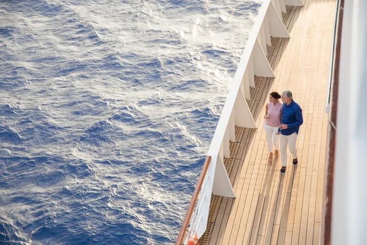 Mature couple strolling on a cruise ship deck with the ocean view, enjoying the sun and fresh air, creating a travel or lifestyle moment.