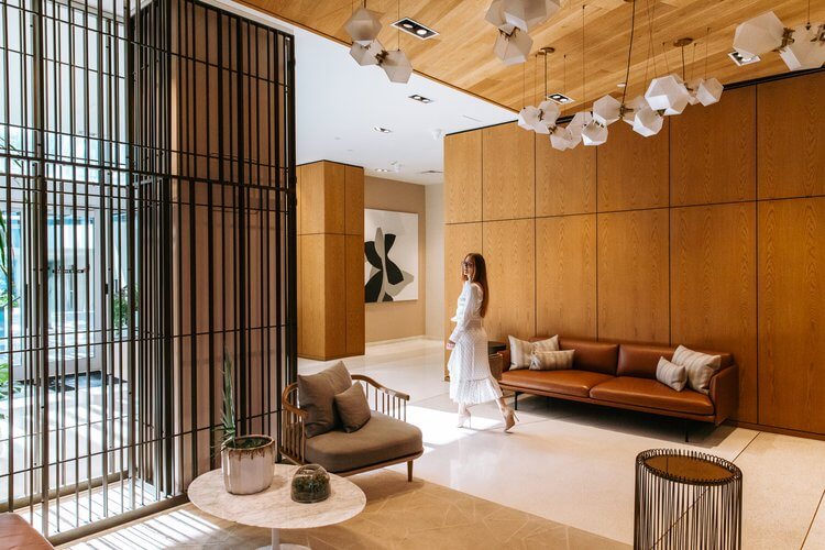 Woman in white dress walks through a modern interior with wood paneling, geometric lighting, and contemporary furniture and decor.