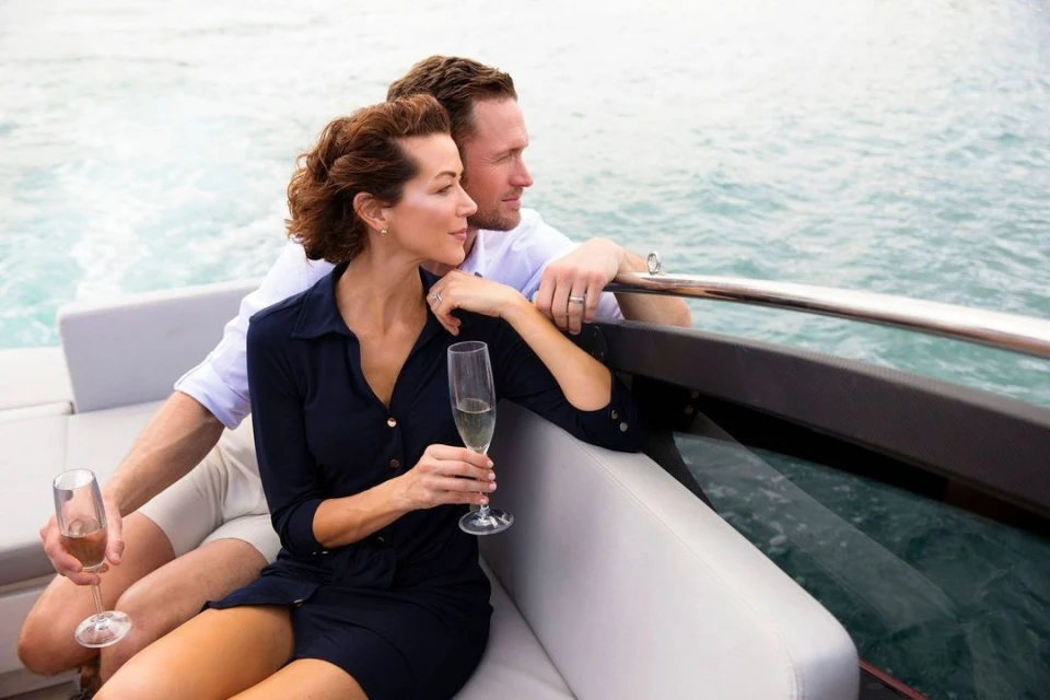Couple enjoys champagne on a boat with ocean backdrop, dressed in casual attire, creating a moment of leisure and sophistication.