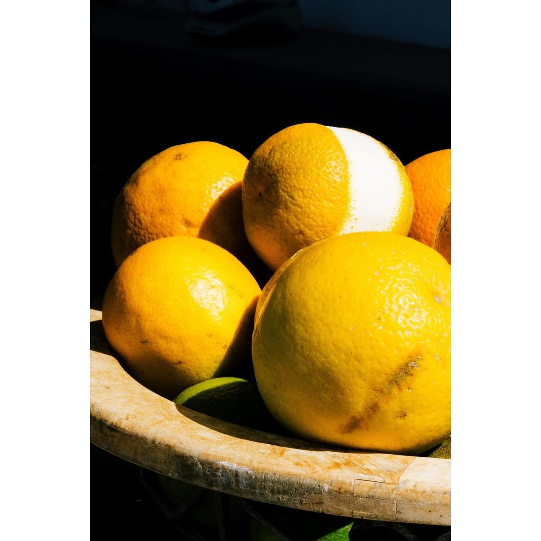 Close-up of a bowl filled with vibrant yellow and green citrus fruits under dramatic lighting, showcasing their textured surfaces and colors.