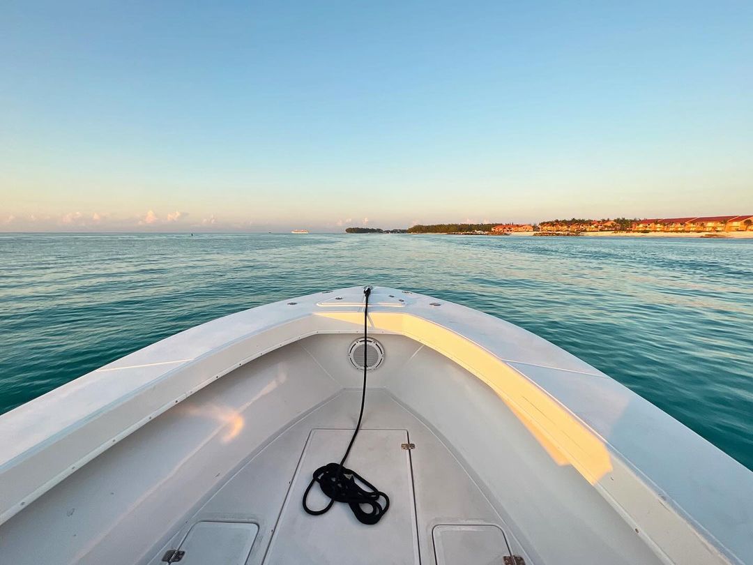 Boat cruising on turquoise water toward a distant shoreline under a clear blue sky, capturing a serene maritime scene.