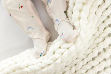 Close-up of a baby's feet in printed footed leggings resting on a chunky white knit blanket.