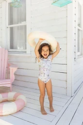 Young child holding a white inflatable ring above head on a white wooden porch by Amanda Julca