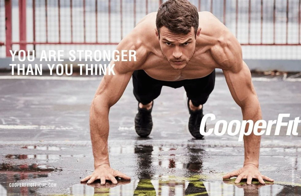 Muscular man in athletic wear is doing a push-up outdoors on a wet surface with arms extended, showcasing fitness and upper body strength.