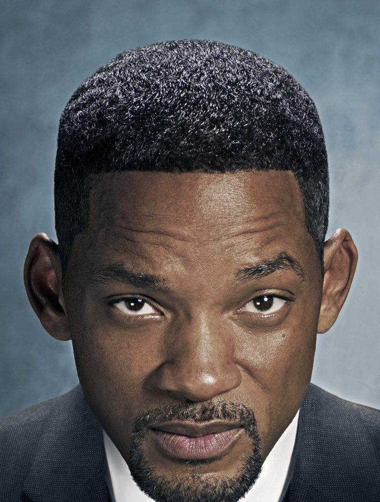 Close-up portrait of a Black adult male with a trimmed beard and suit jacket, looking directly at the camera with a serious expression.