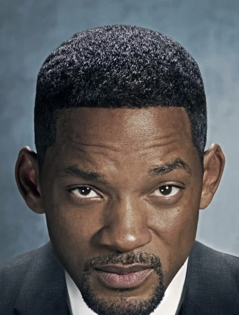 Close-up portrait of a Black adult male with a trimmed beard and suit jacket, looking directly at the camera with a serious expression.