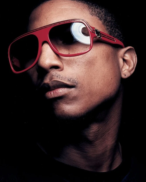 Close-up portrait of a dark-skinned adult male wearing red sunglasses against a dark background in a studio setting.