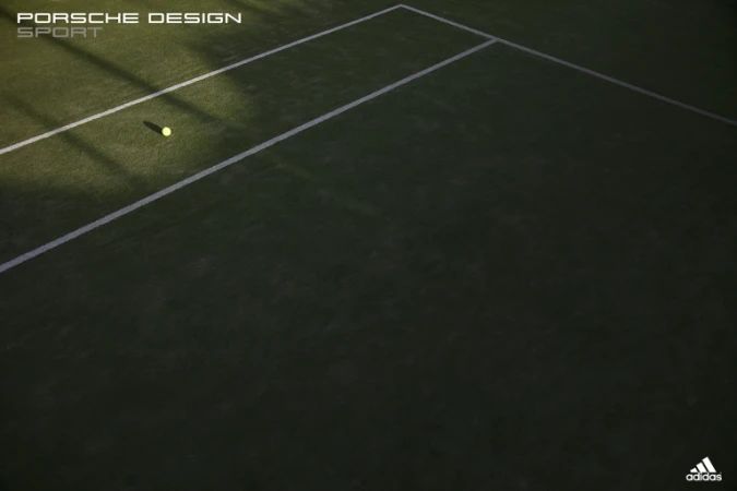 High angle shot of a tennis ball resting on a green tennis court with white boundary lines under low light.