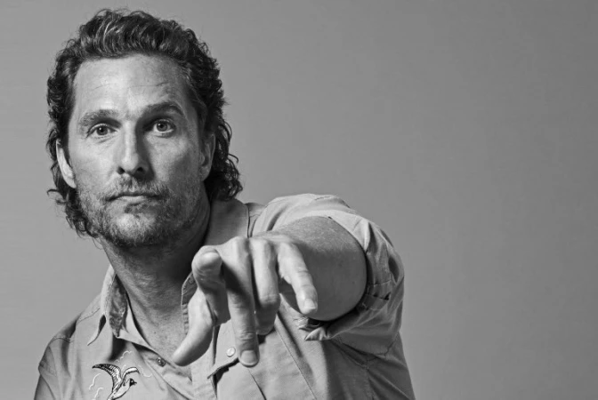Black and white portrait of Matthew McConaughey pointing directly at the camera while wearing an embroidered shirt