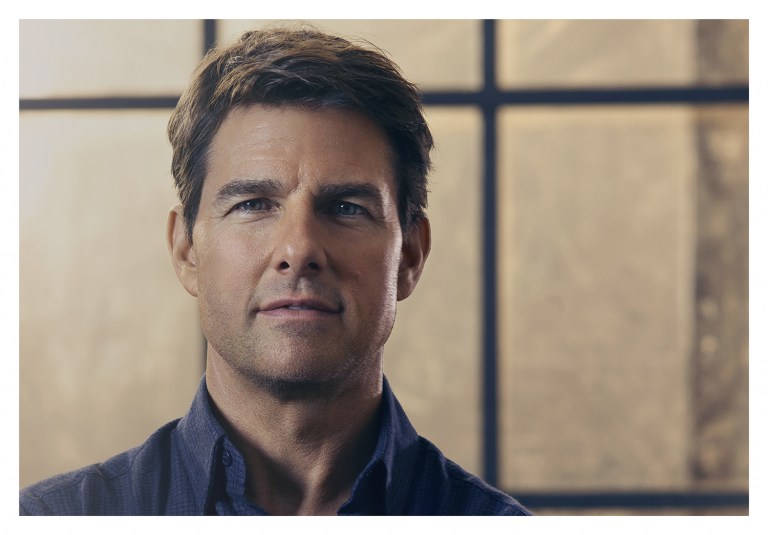 Portrait of Tom Cruise in a dark patterned shirt against a blurred window backdrop by photographer James Dimmock.