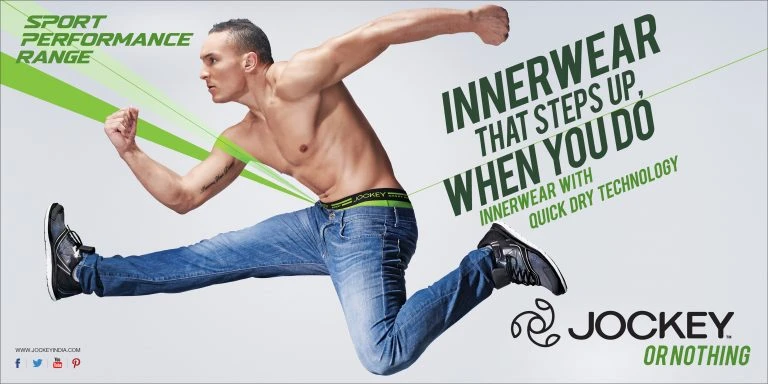 Athletic man in motion wearing jeans and Jockey underwear for a sportswear campaign on a white background with green accents and text.