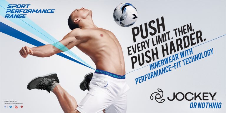 Athlete in athletic wear jumps with a soccer ball against a light background in a Jockey brand advertisement for sport performance.