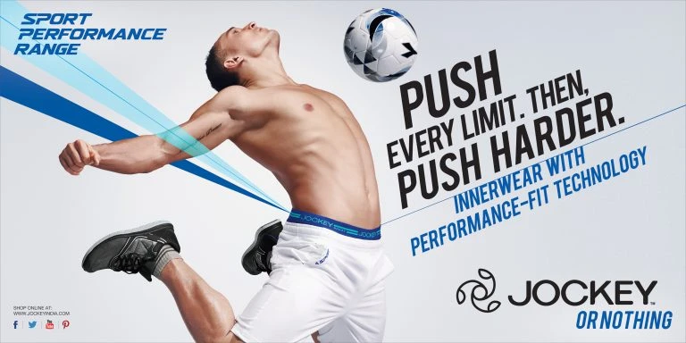 Athlete in athletic wear jumps with a soccer ball against a light background in a Jockey brand advertisement for sport performance.