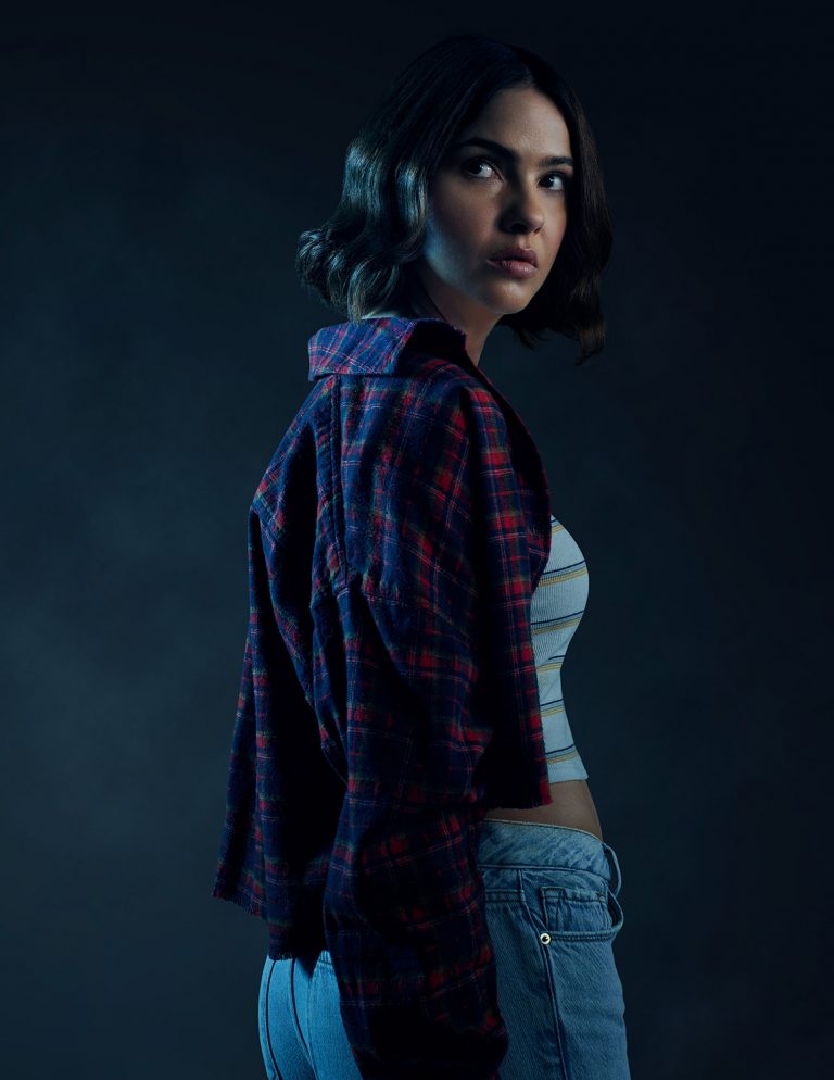 Woman with dark short hair wearing a red plaid overshirt and blue jeans glancing over her shoulder