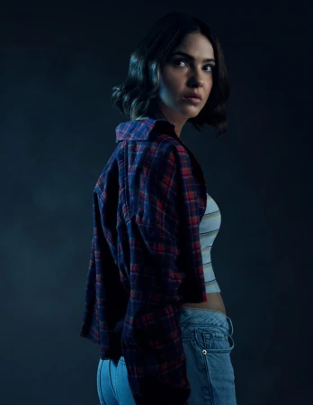 Woman with dark short hair wearing a red plaid overshirt and blue jeans glancing over her shoulder