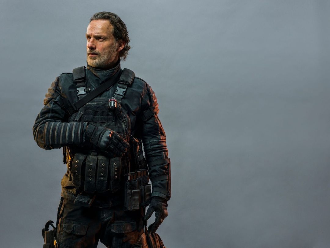 Man in tactical gear stands in a gray studio. Adult male poses with a serious expression in front of plain background with soft lighting.