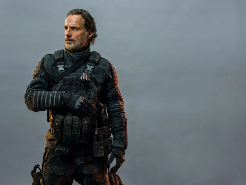 Man in tactical gear stands in a gray studio. Adult male poses with a serious expression in front of plain background with soft lighting.