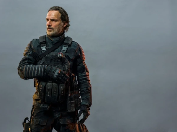 Man in tactical gear stands in a gray studio. Adult male poses with a serious expression in front of plain background with soft lighting.