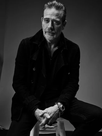 Portrait of Jeffrey Dean Morgan seated on a stool wearing a dark jacket against a grey seamless background