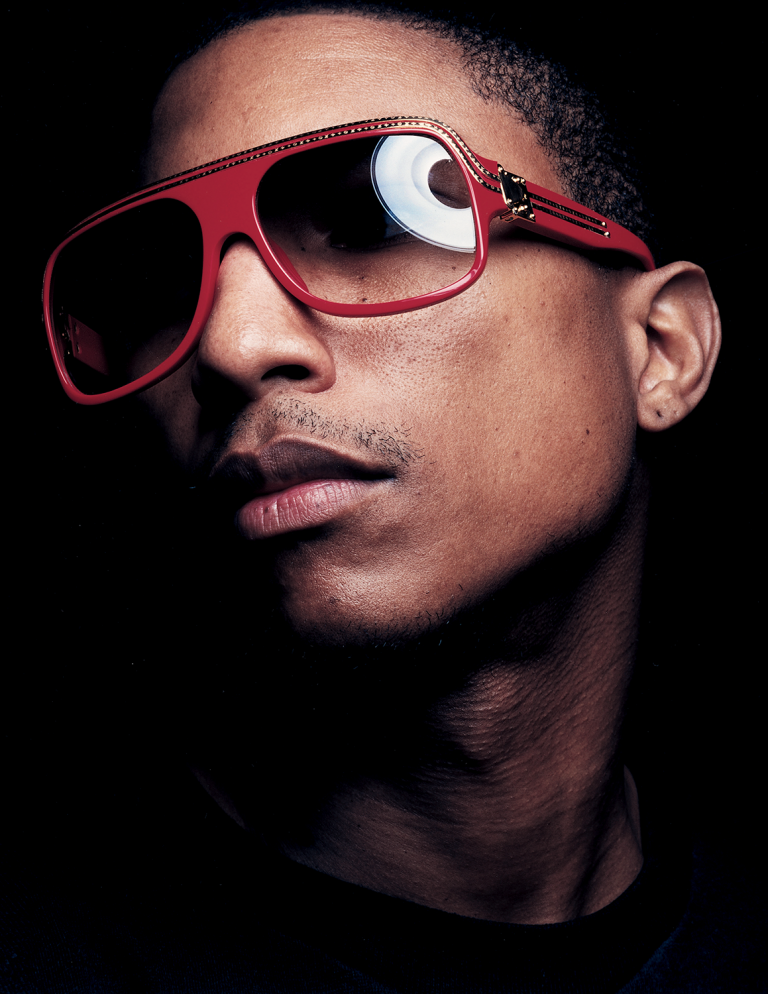 Close-up portrait of a person with dark skin wearing stylish red sunglasses against a dark background with diffused studio lighting.