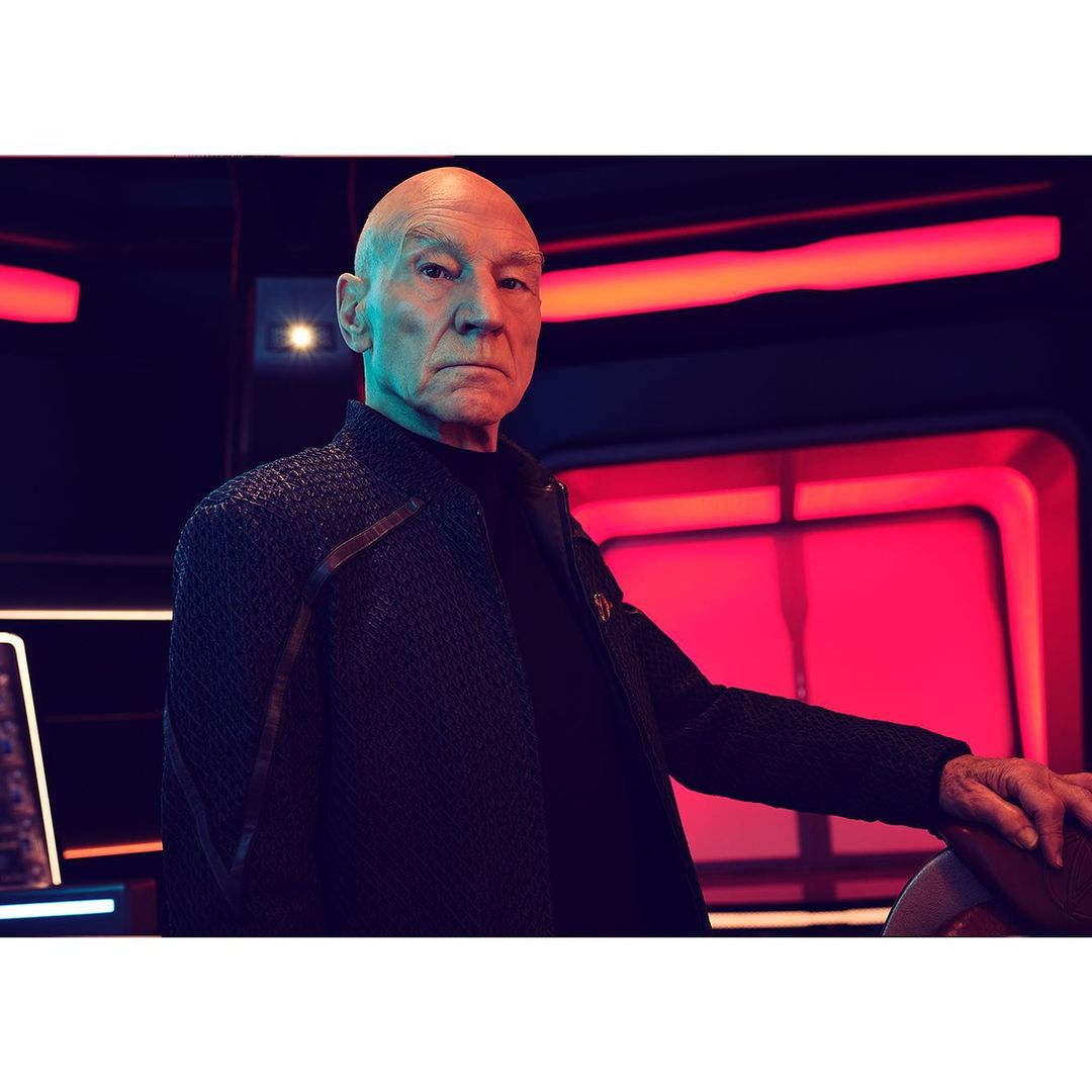 Portrait of Patrick Stewart in Star Trek costume, posing indoors with futuristic background, in a medium shot with dramatic lighting.