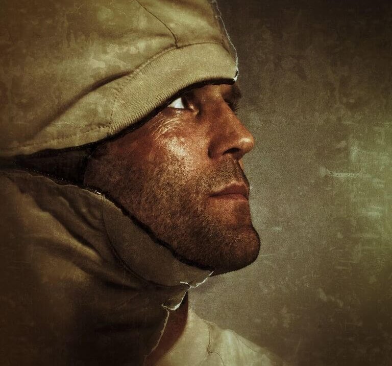 Close-up studio portrait of a man with a hooded jacket, looking up and away. The neutral background enhances the focus on the subject.
