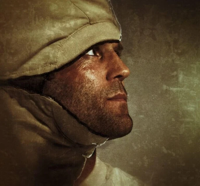 Close-up studio portrait of a man with a hooded jacket, looking up and away. The neutral background enhances the focus on the subject.