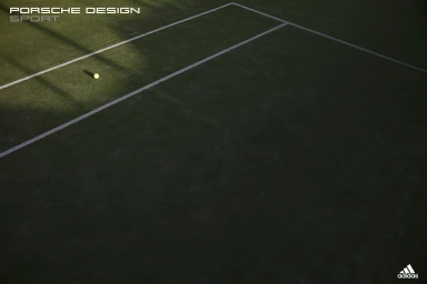 High angle shot of a tennis ball resting on a green tennis court with white boundary lines under low light.