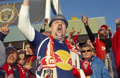 Soccer fan in hard hat and scarf cheering in crowd by James Dimmock