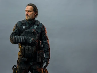 Portrait of Andrew Lincoln wearing tactical gear and black vest against a plain grey background