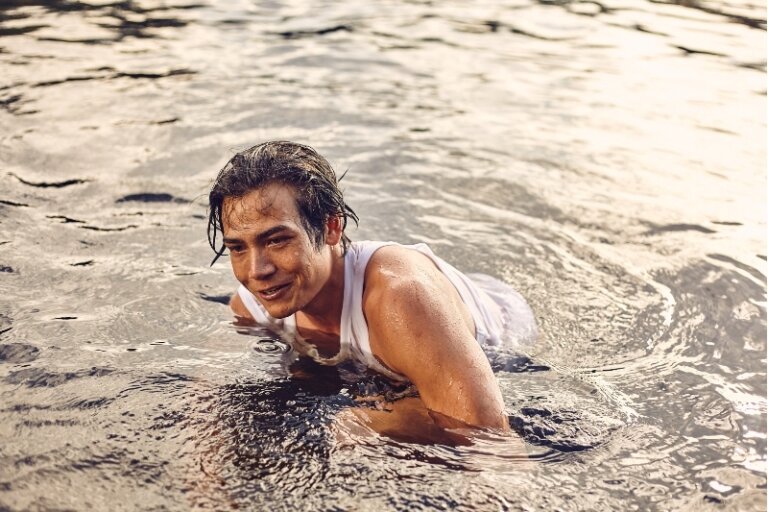 Wet man in white tank top swimming in a natural body of water captured by Coty Tarr