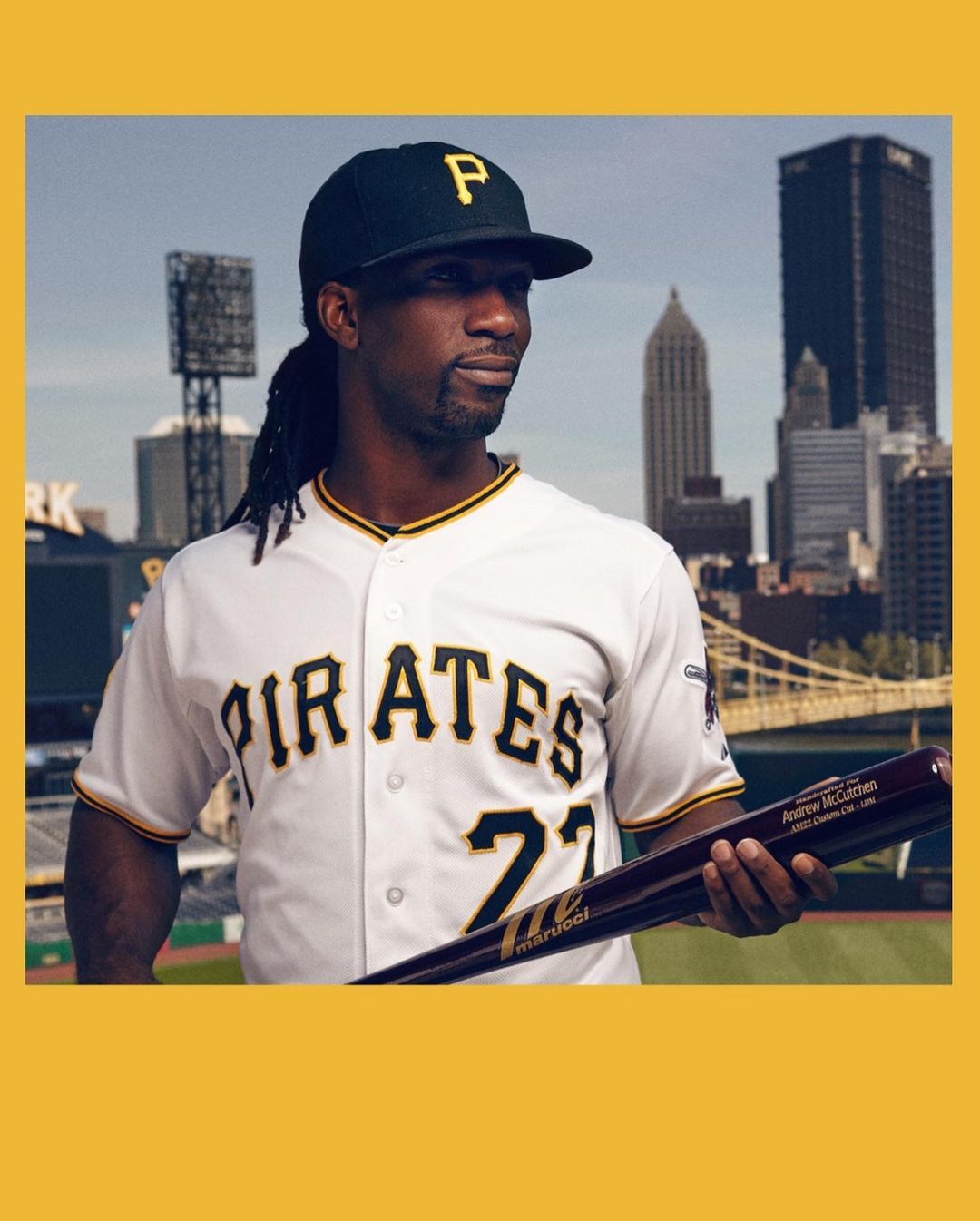 Portrait of professional baseball player in uniform with baseball bat standing against an urban backdrop with modern buildings.