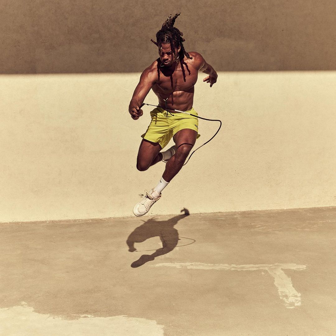Athletic Black man jumps with a jump rope outdoors. He wears yellow shorts and white athletic shoes, performing fitness exercise.
