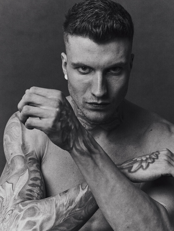 Monochrome portrait of a tattooed man with short hair holding his fists up in a fighting pose