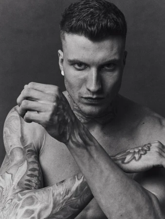 Monochrome portrait of a tattooed man with short hair holding his fists up in a fighting pose