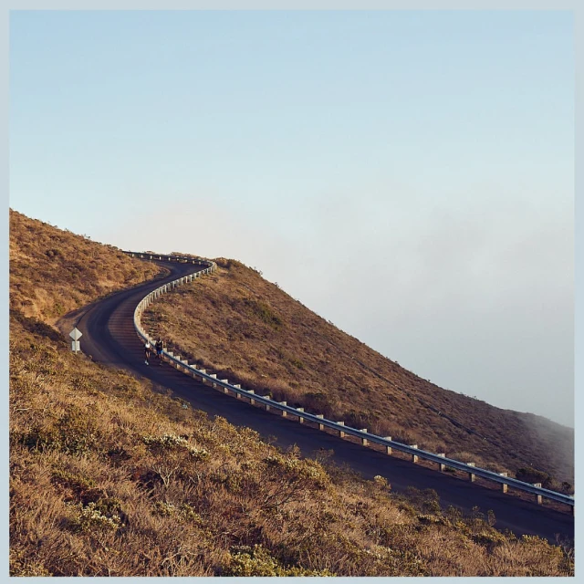 Winding road curves up a grassy hillside under a clear sky, showcasing a scenic drive with natural beauty and open sky above.