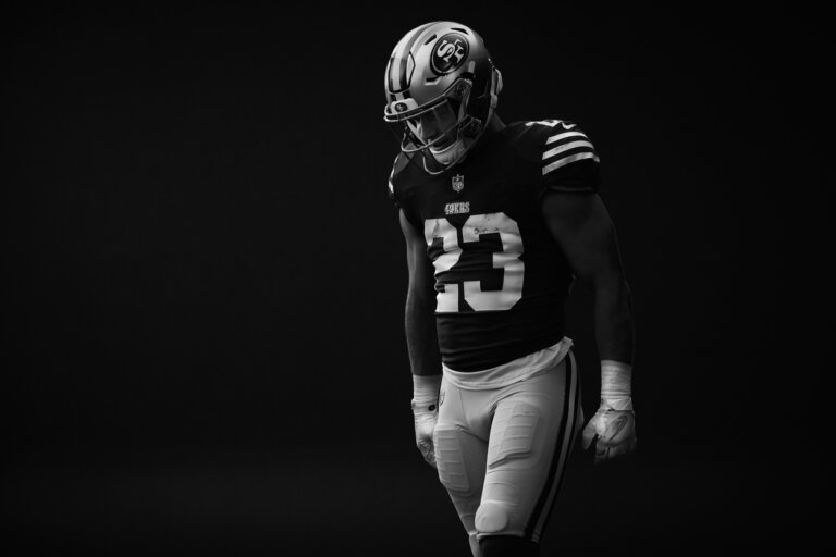 Monochrome image of a male football player in uniform with helmet, pads, and the number 23, against a dark background.