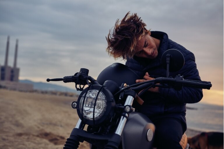 Man sitting on a dark motorcycle at the beach during sunset, photographed by Coty Tarr.