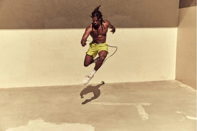 Athletic, shirtless man jumping rope in an indoor space with cream-colored walls and concrete floors, demonstrating fitness and athleticism.