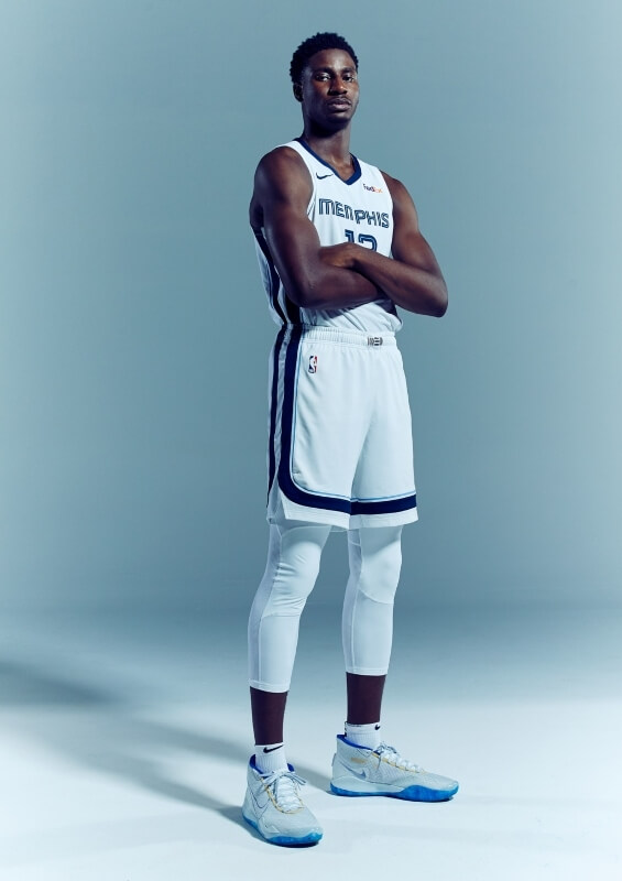 Full-length portrait of a basketball player in a white Memphis Grizzlies uniform, standing in a studio with arms crossed.