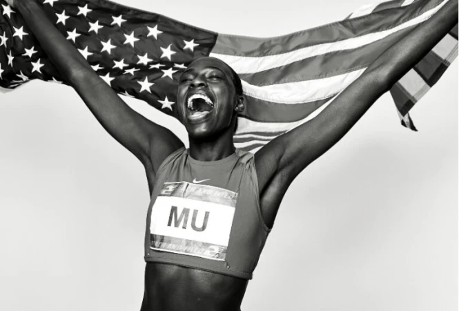 Black and white portrait of a female athlete holding an American flag and celebrating a victory, wearing a sports uniform.