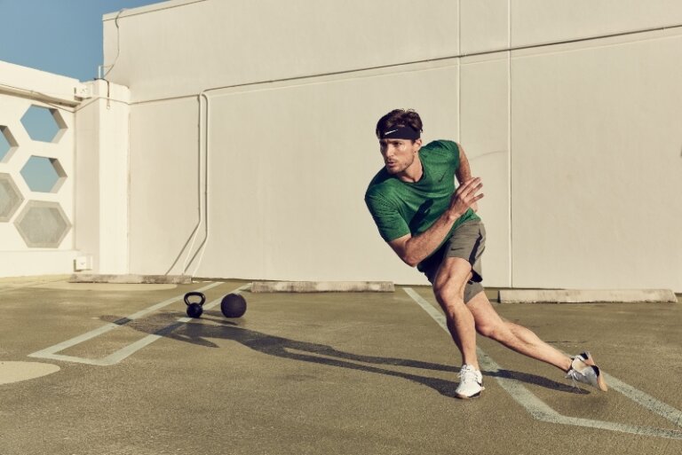 Athletic man in sportswear, headband, and trainers in motion, exercising outdoors with kettlebell and medicine ball.