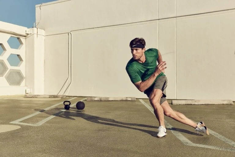 Athletic man in sportswear, headband, and trainers in motion, exercising outdoors with kettlebell and medicine ball.