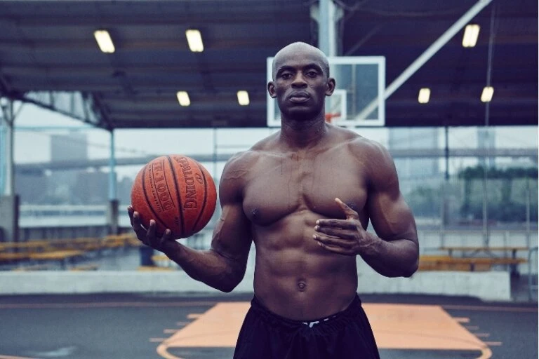 Athletic man holding basketball on outdoor court. Close-up shot of muscular, shirtless male athlete with ball. Urban basketball court.