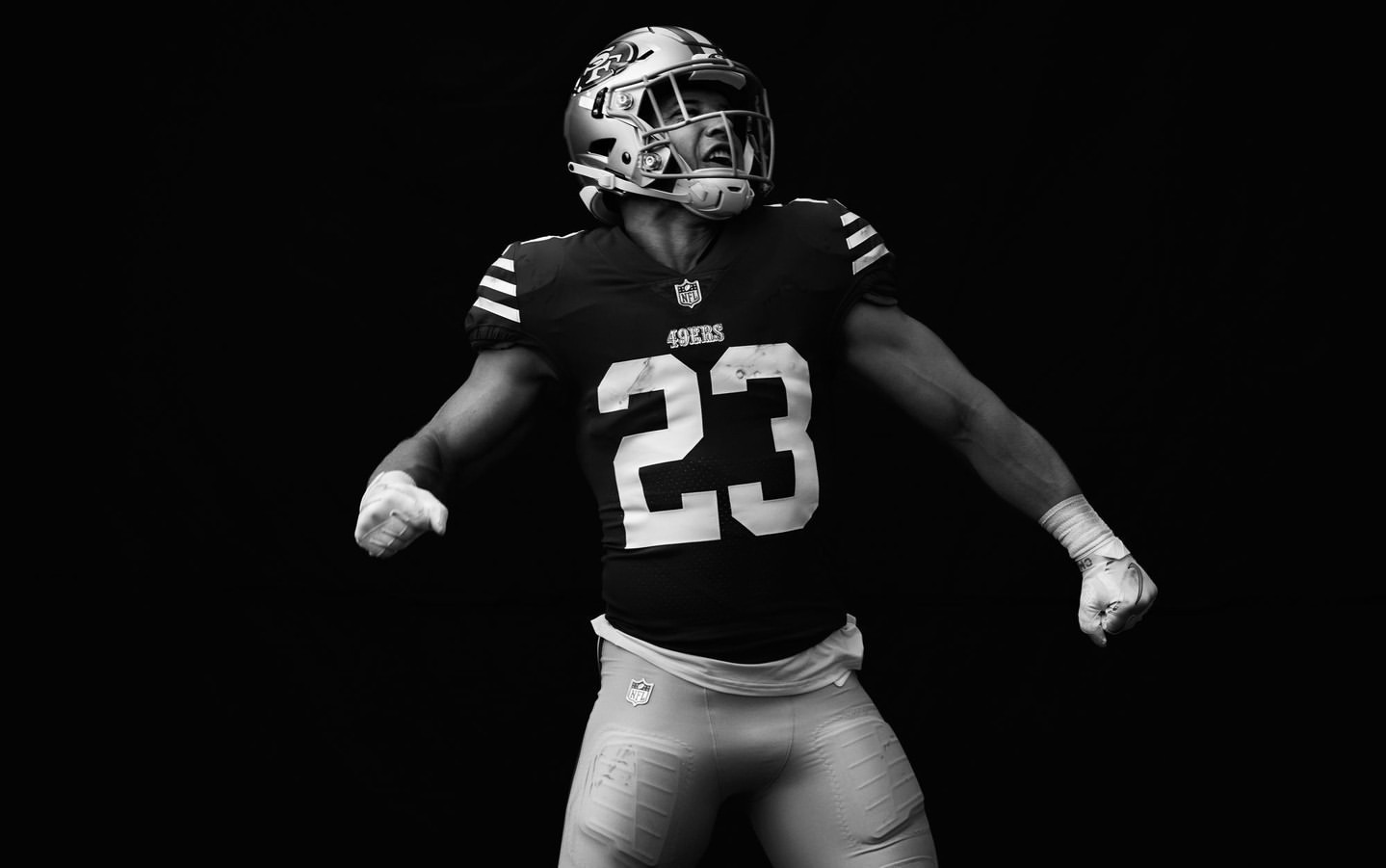 Black and white portrait of a football player in uniform with helmet, number 23 on jersey, looking upwards against a black background.